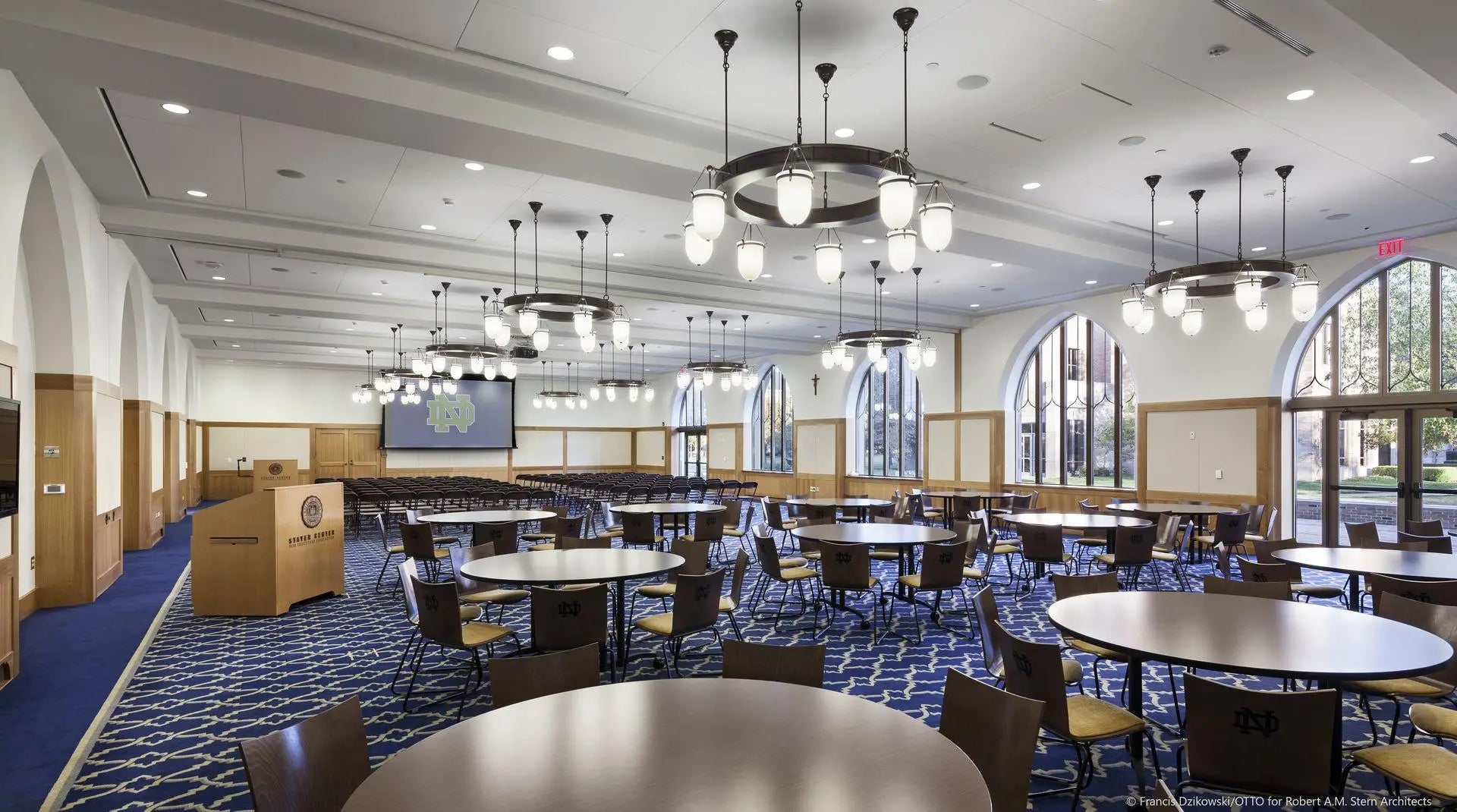 A large event hall at the university of notre dame stayer center with round and oval tables and decorative chandeliers