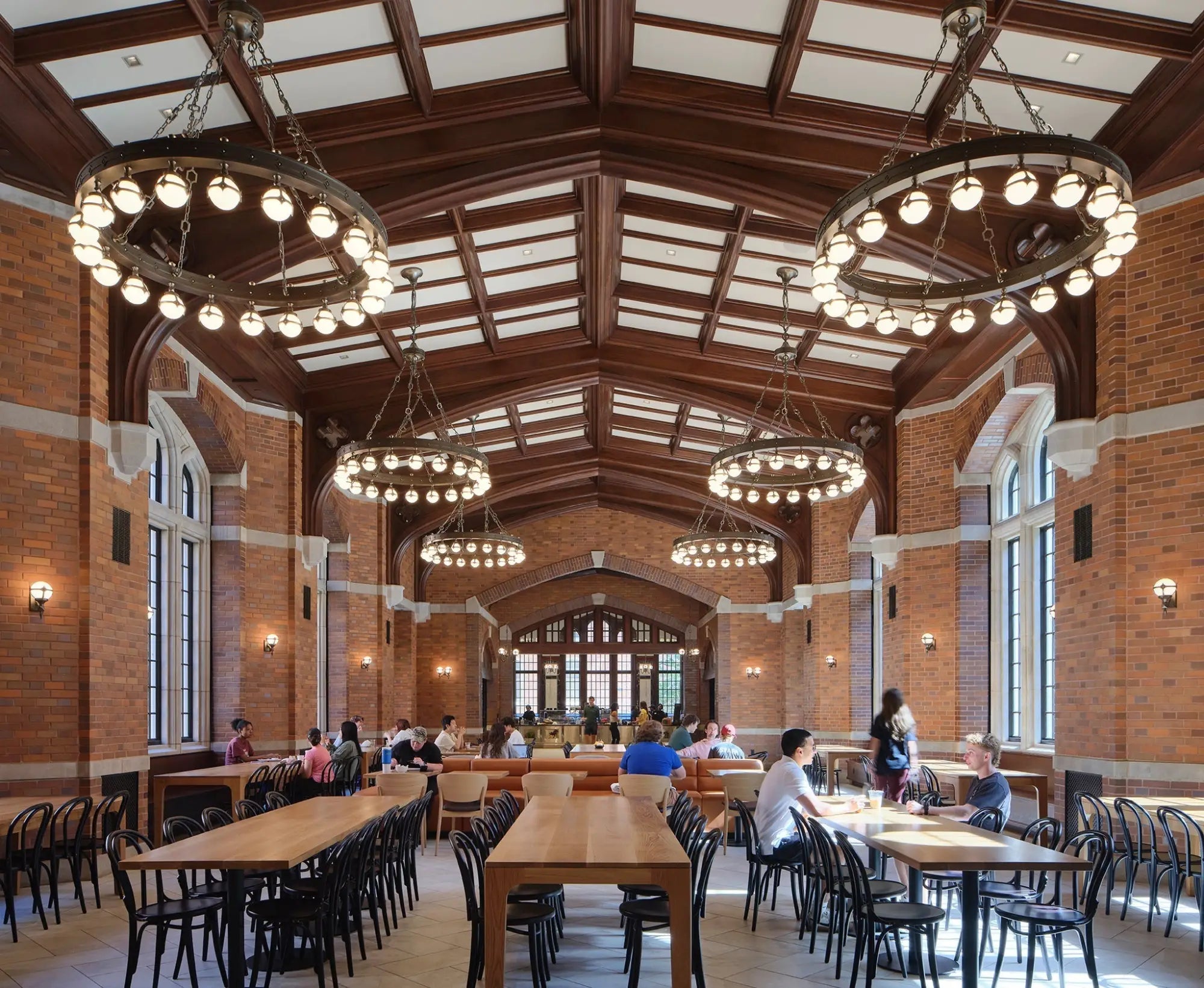 A spacious dining hall at Vanderbilt University featuring long wooden tables, black chairs, and ornate circular chandeliers.