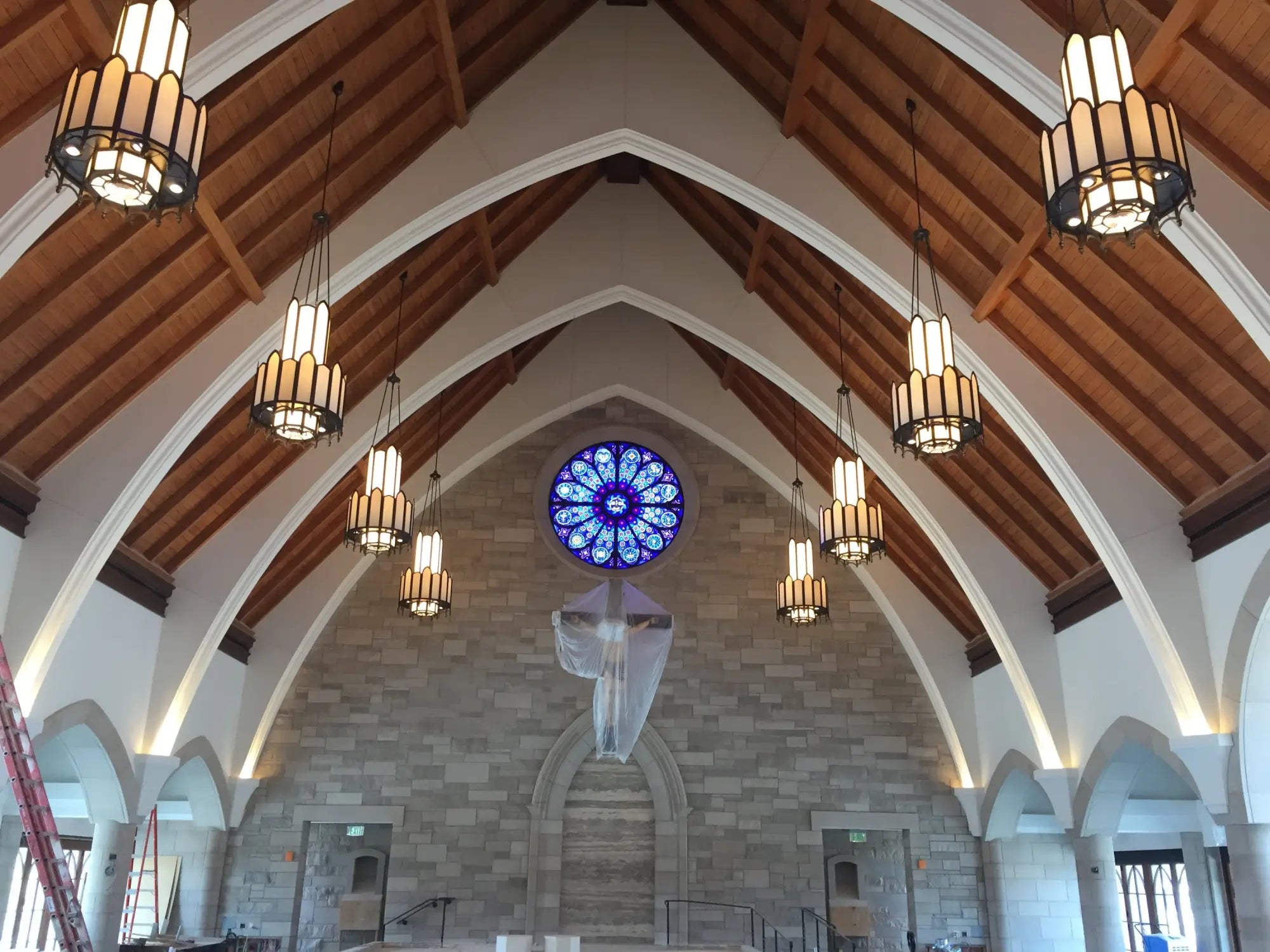 Wooden arched ceiling with hanging pendant lights and stained glass window.