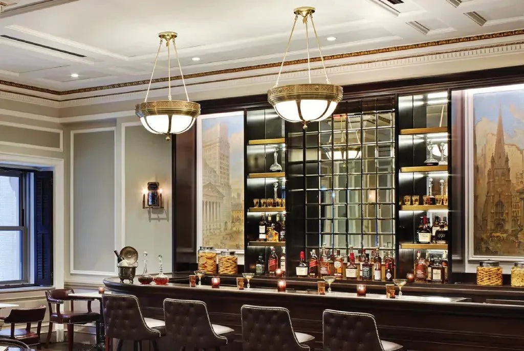 Buttonwood pendant featuring two large globe lights over a fully stocked dark wood bar with upholstered stools and mirrored wall
