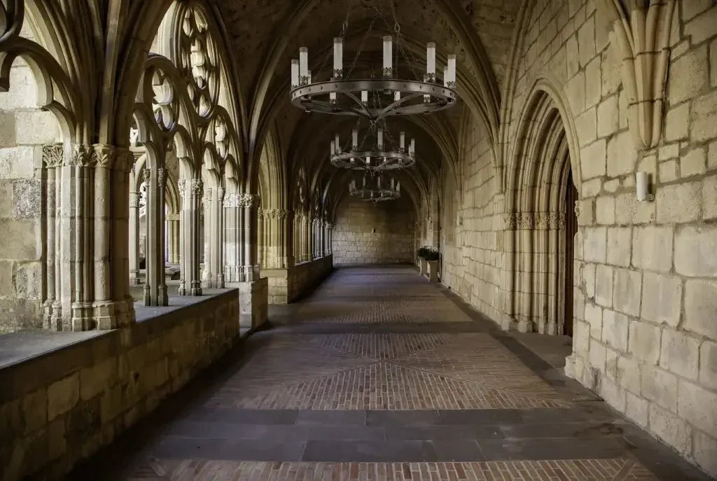 Skellig chandelier hanging in a long stone hallway with arched columns and ornate windows in a classic setting