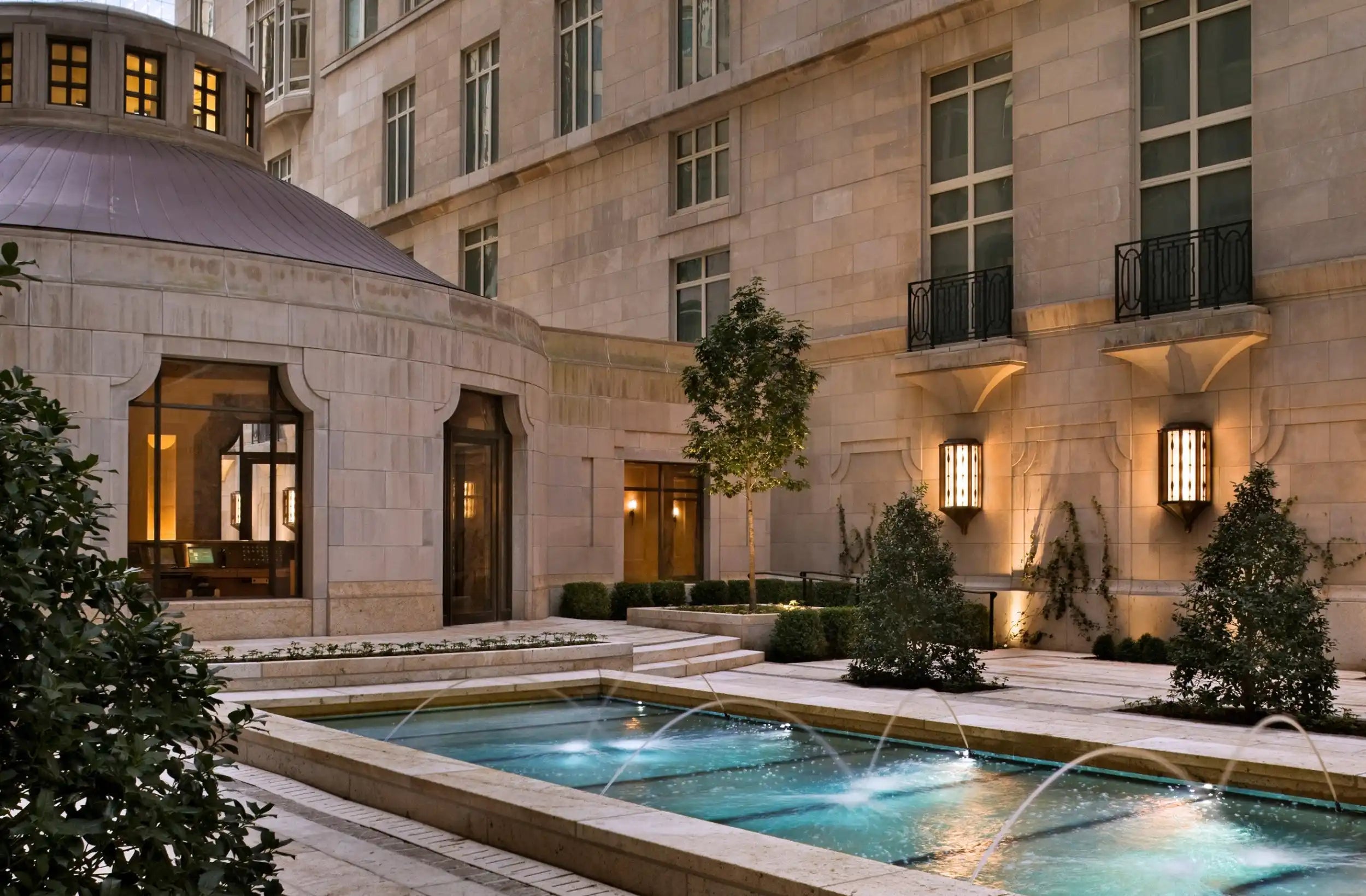 Elegant outdoor courtyard with a rectangular water feature and fountains, surrounded by a stone building.
