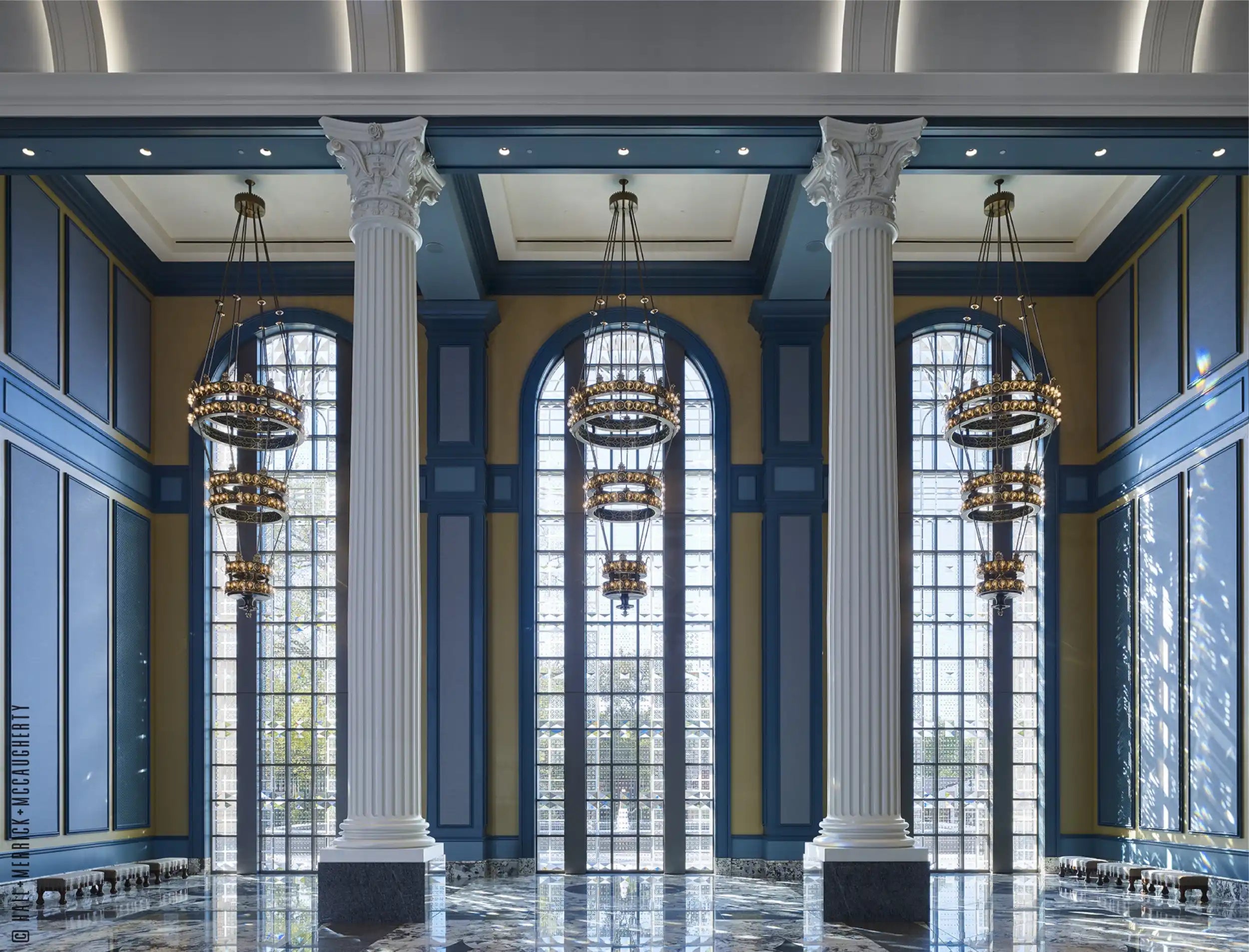 An expansive hall with tall windows, grand pillars, and multi-tiered chandeliers.