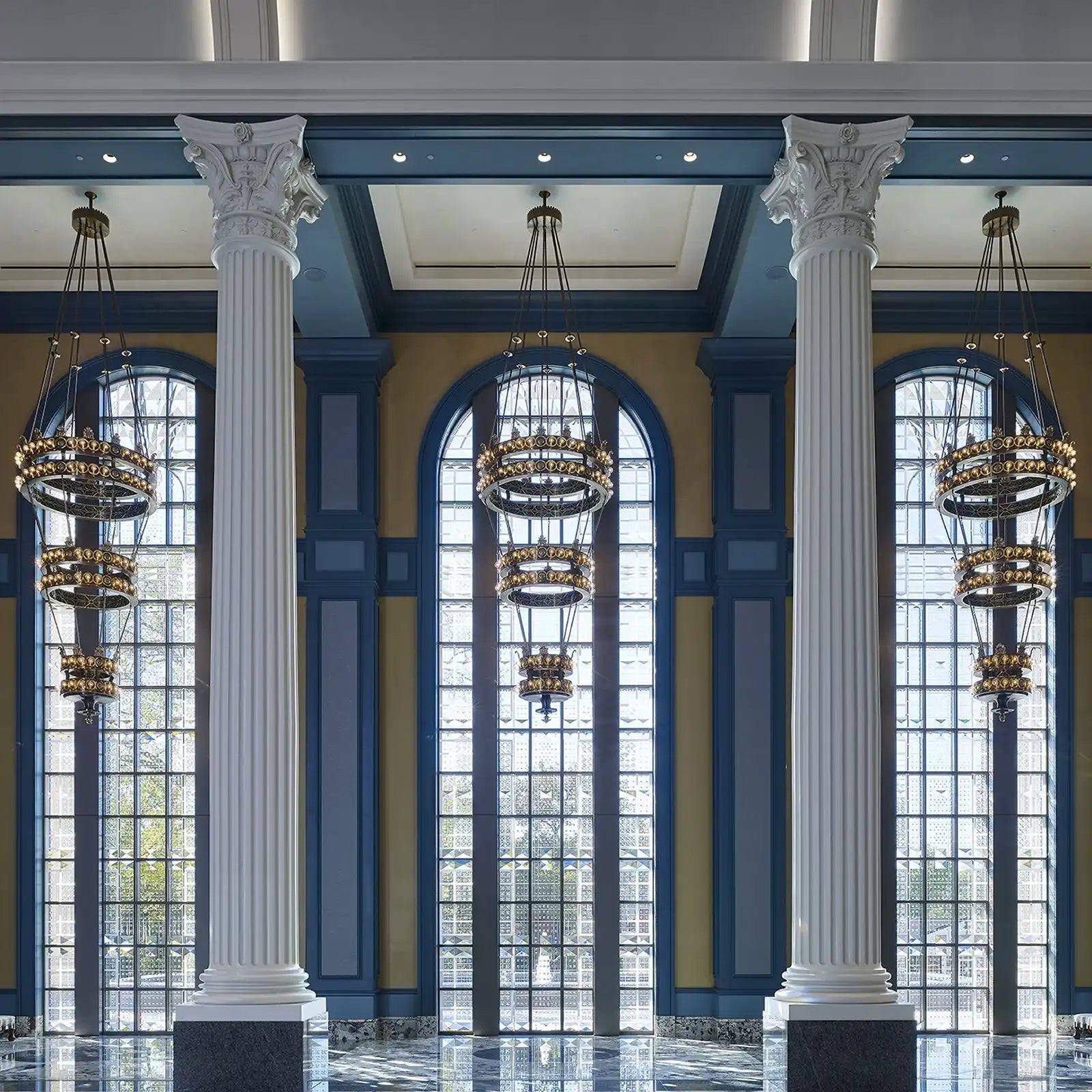 A grand hall with tall arched windows, ornate chandeliers, and classical columns.