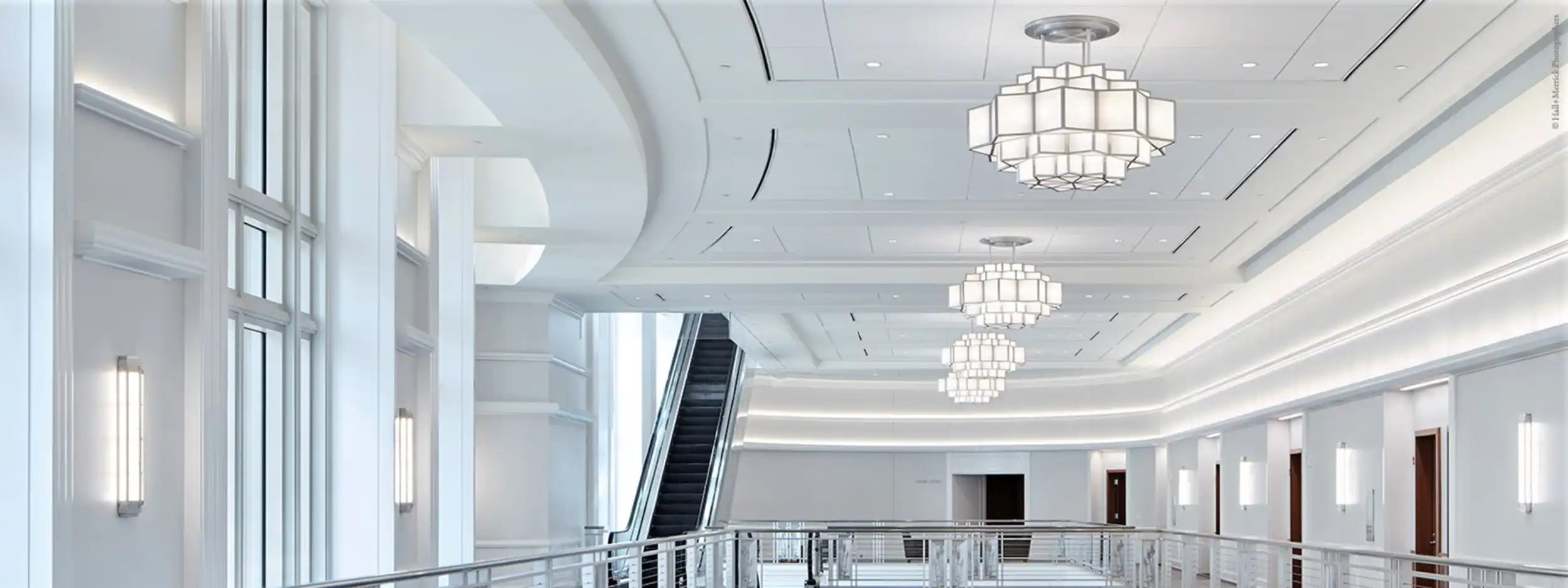 A long, brightly lit hallway with multiple chandeliers and an escalator.