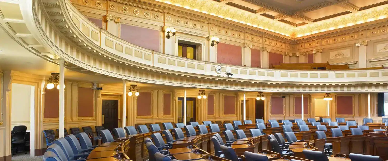 An ornate, curved legislative chamber with blue seating and a balcony.