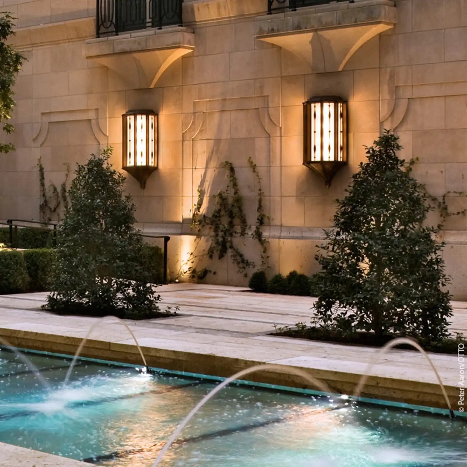 A stone wall with two illuminated, ornate sconces and climbing vines.