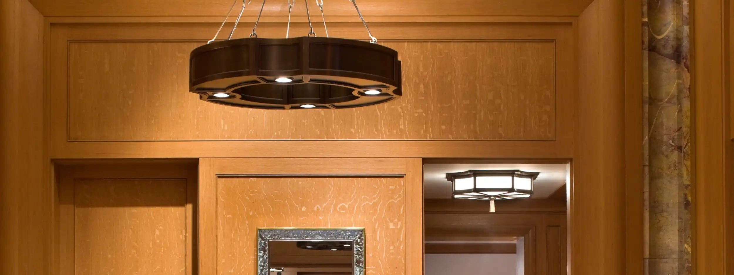 A dark, circular chandelier with exposed bulbs and a decorative silver frame.