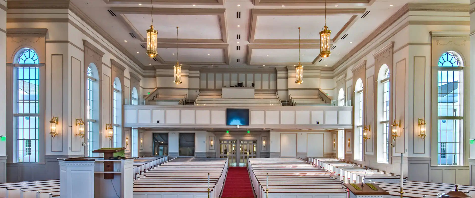 An empty church sanctuary with rows of white pews and a red carpet aisle.