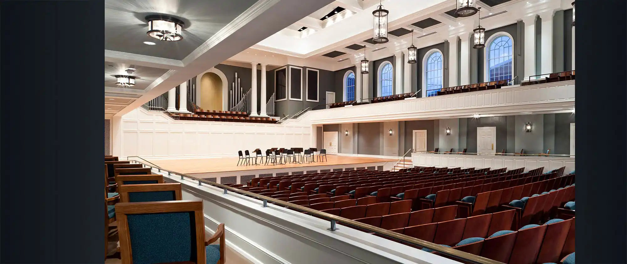 A grand concert hall with an organ, upper balcony seating, and a main floor of red-upholstered seats.