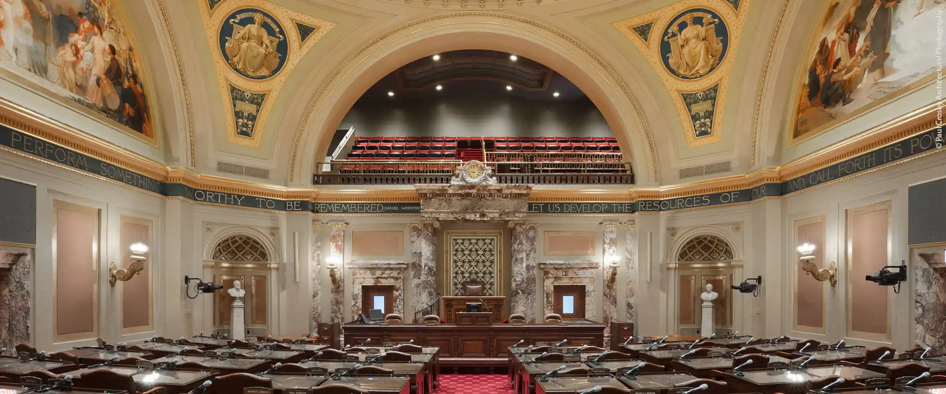 A grand, ornate legislative chamber with rows of wooden desks.