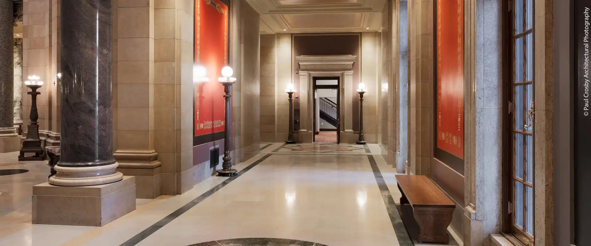 A long, elegant hallway with polished floors, decorative columns, and warm lighting.