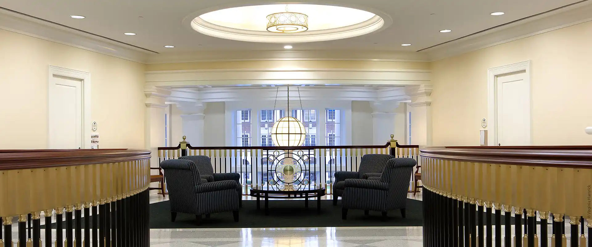 An inviting lounge area with four armchairs and a coffee table, situated on a mezzanine overlooking a grand hall.
