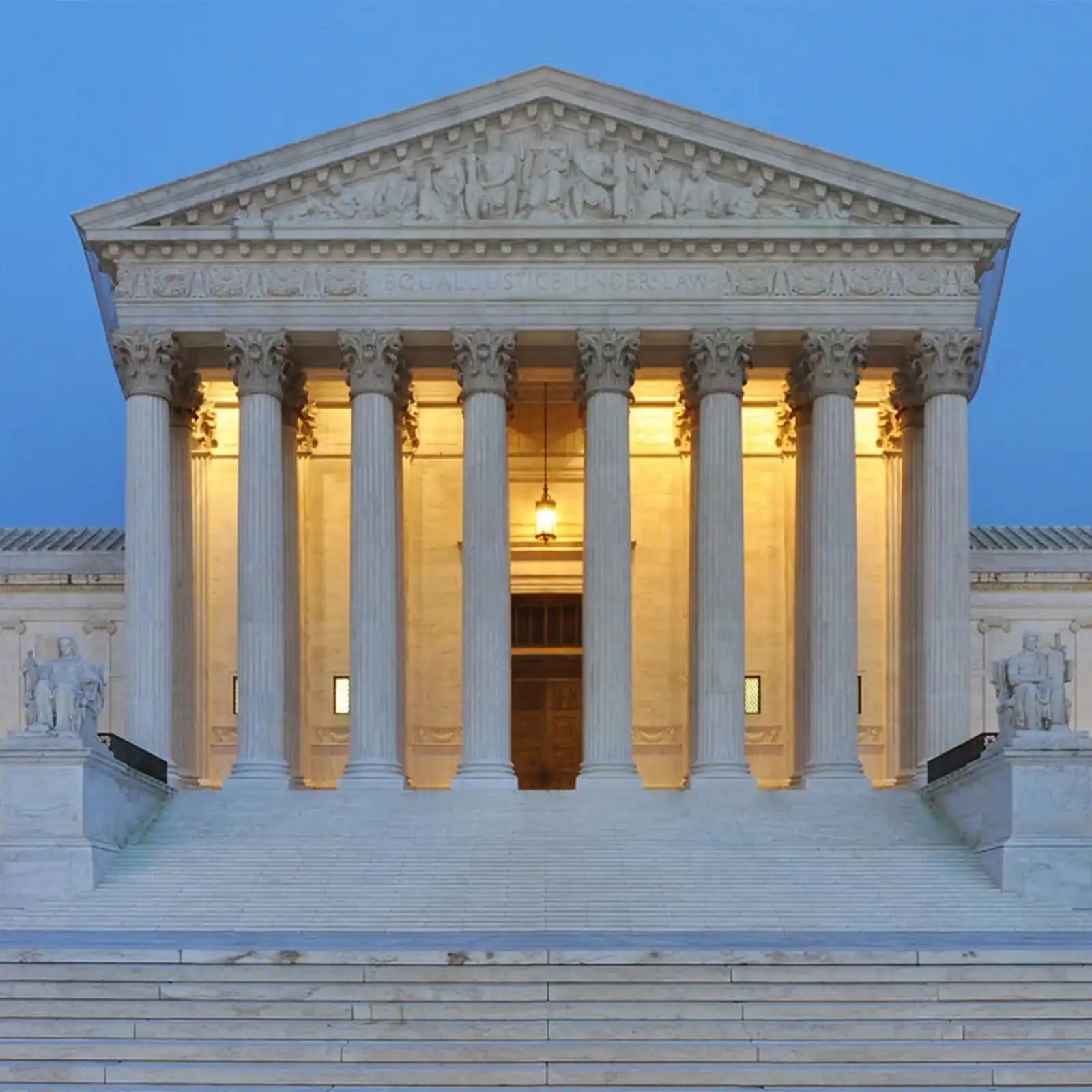 A stately white marble building with tall columns and a grand staircase, illuminated at dusk.