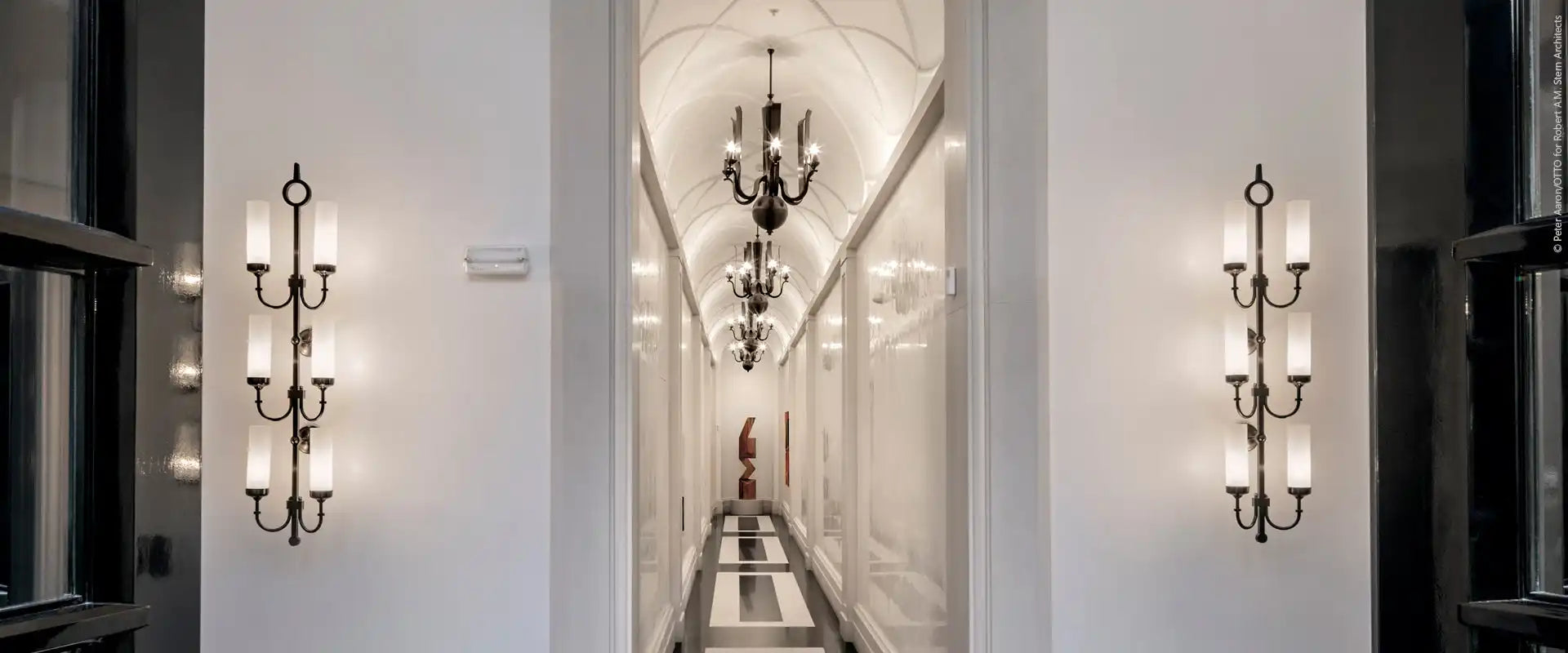 A well-lit, luxurious hallway with ornate wall sconces and chandeliers.